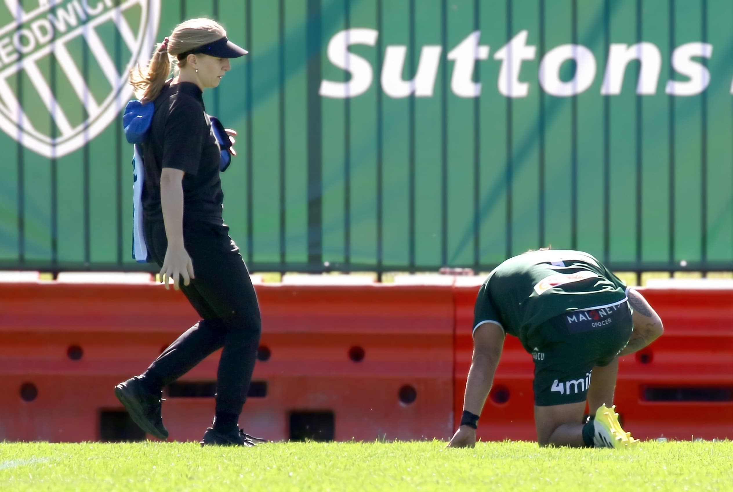 A physio walking onto a pitch toward a player kneeling on the grass